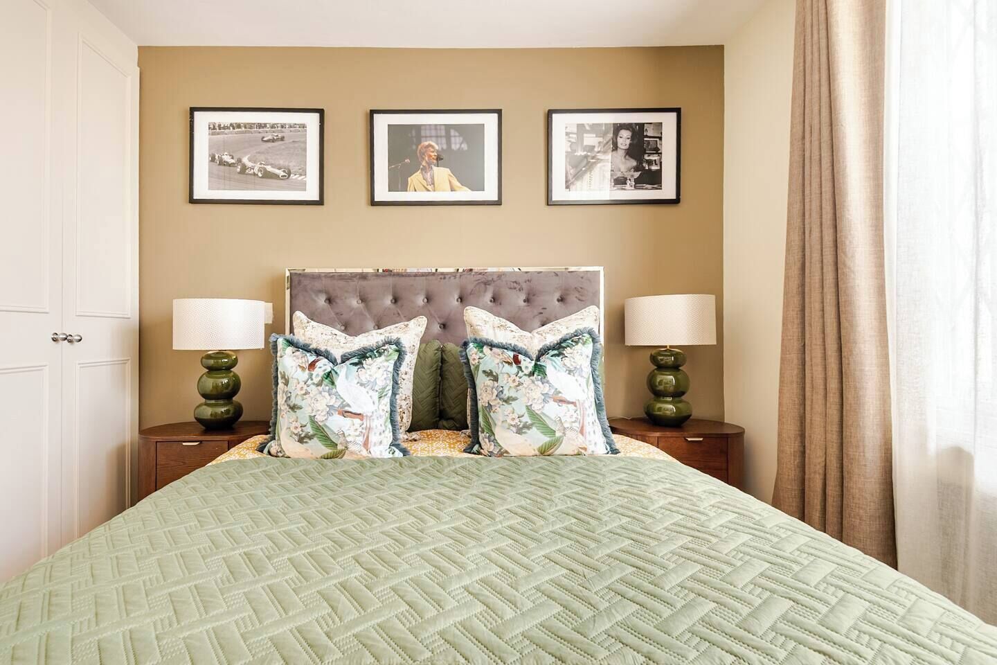 Quarto de hotel com uma cama grande, duas mesas de cabeceira, um painel de cabeceira estofado e três quadros na parede.