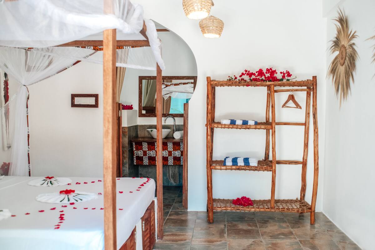 Una habitación con cama, estante de madera con objetos decorativos y espejo.