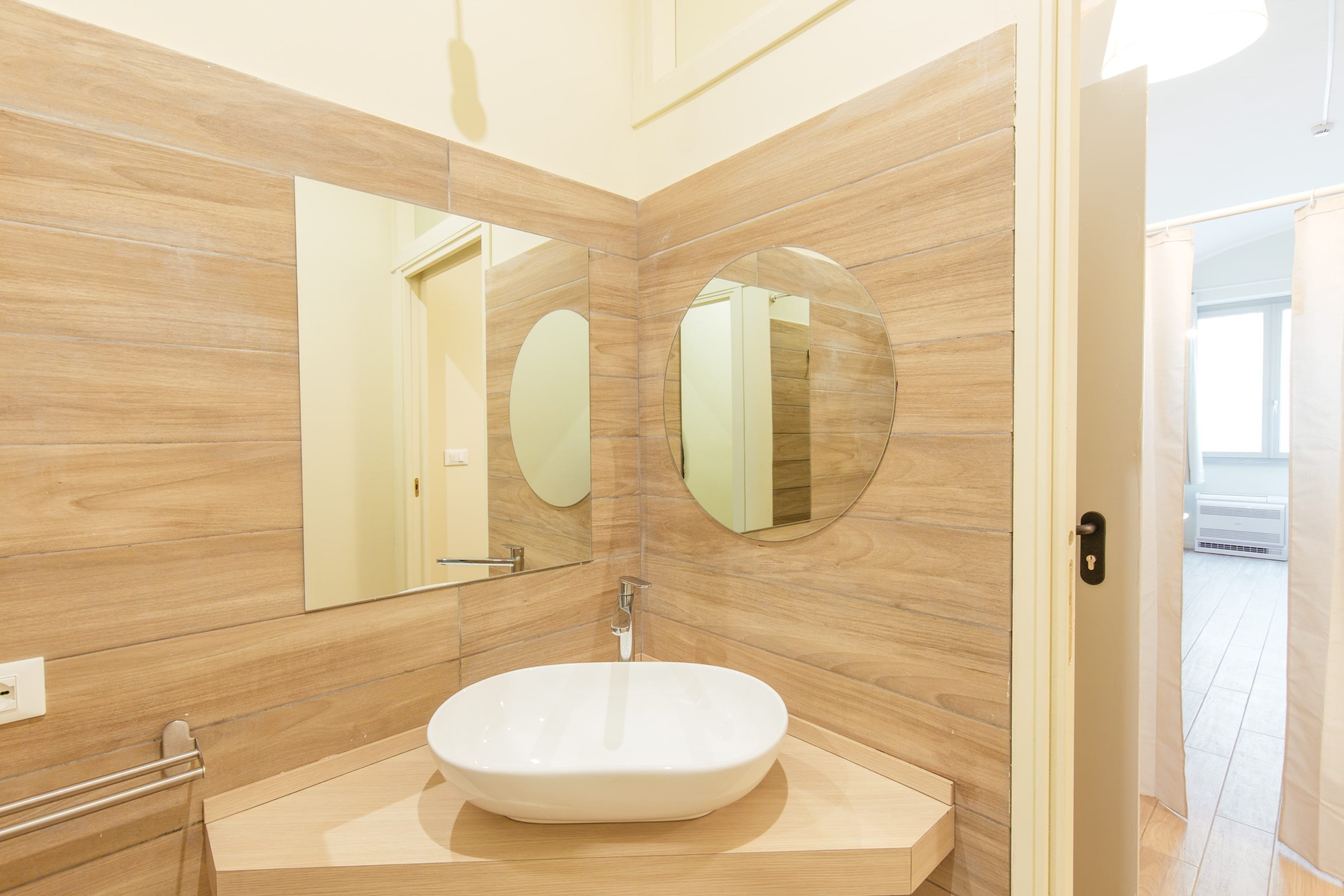 Ein modernes Badezimmer mit einem großen, ovalen Waschbecken, zwei runden Spiegeln und Holzvertäfelung.