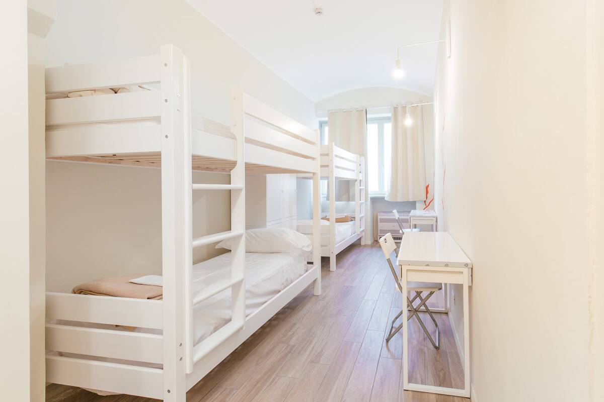 Une chambre avec un lit superposé, un bureau et une chaise, un plancher en bois et une fenêtre avec des rideaux.