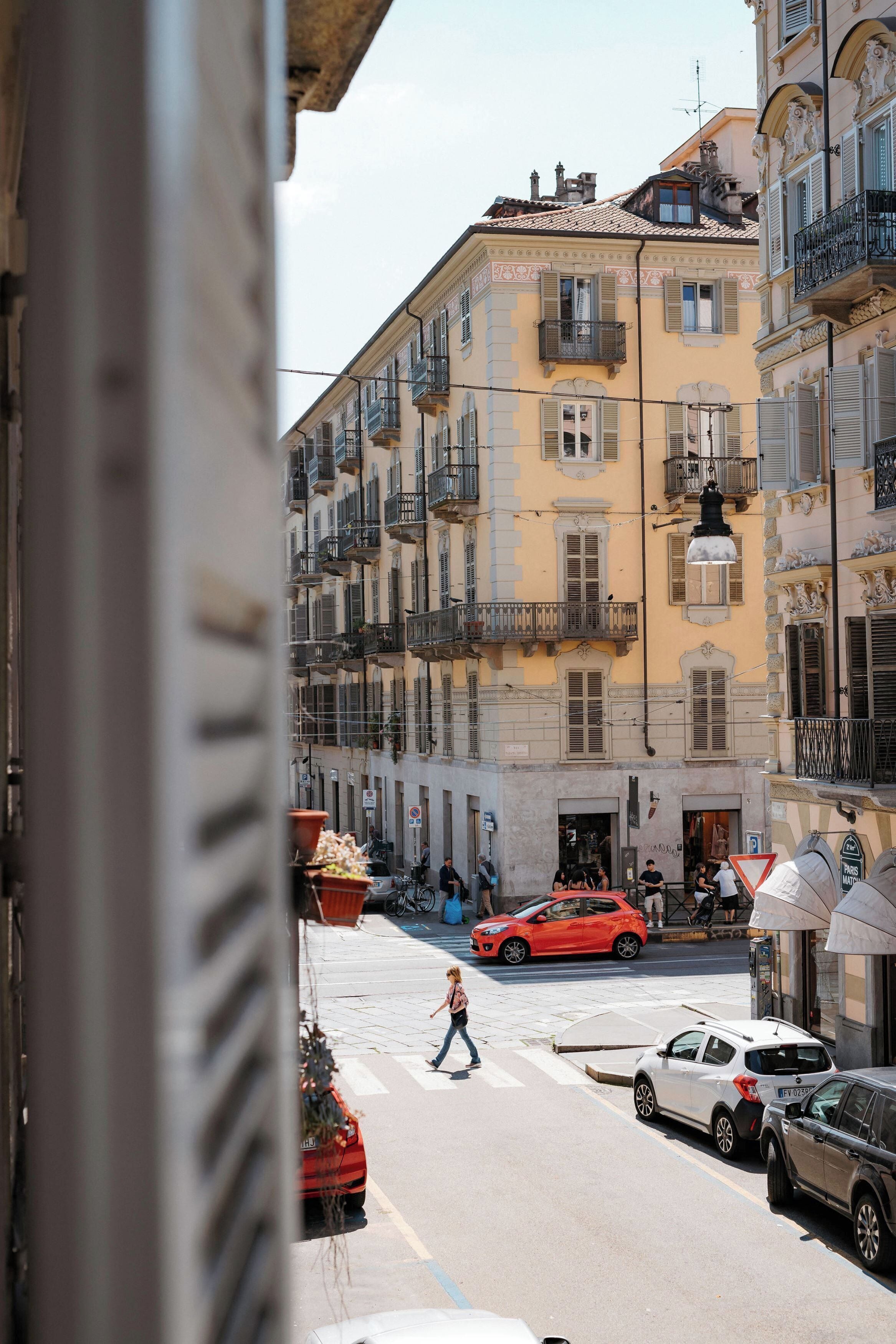 Una vista di una strada con un attraversamento pedonale, auto parcheggiate e palazzi con balconi.