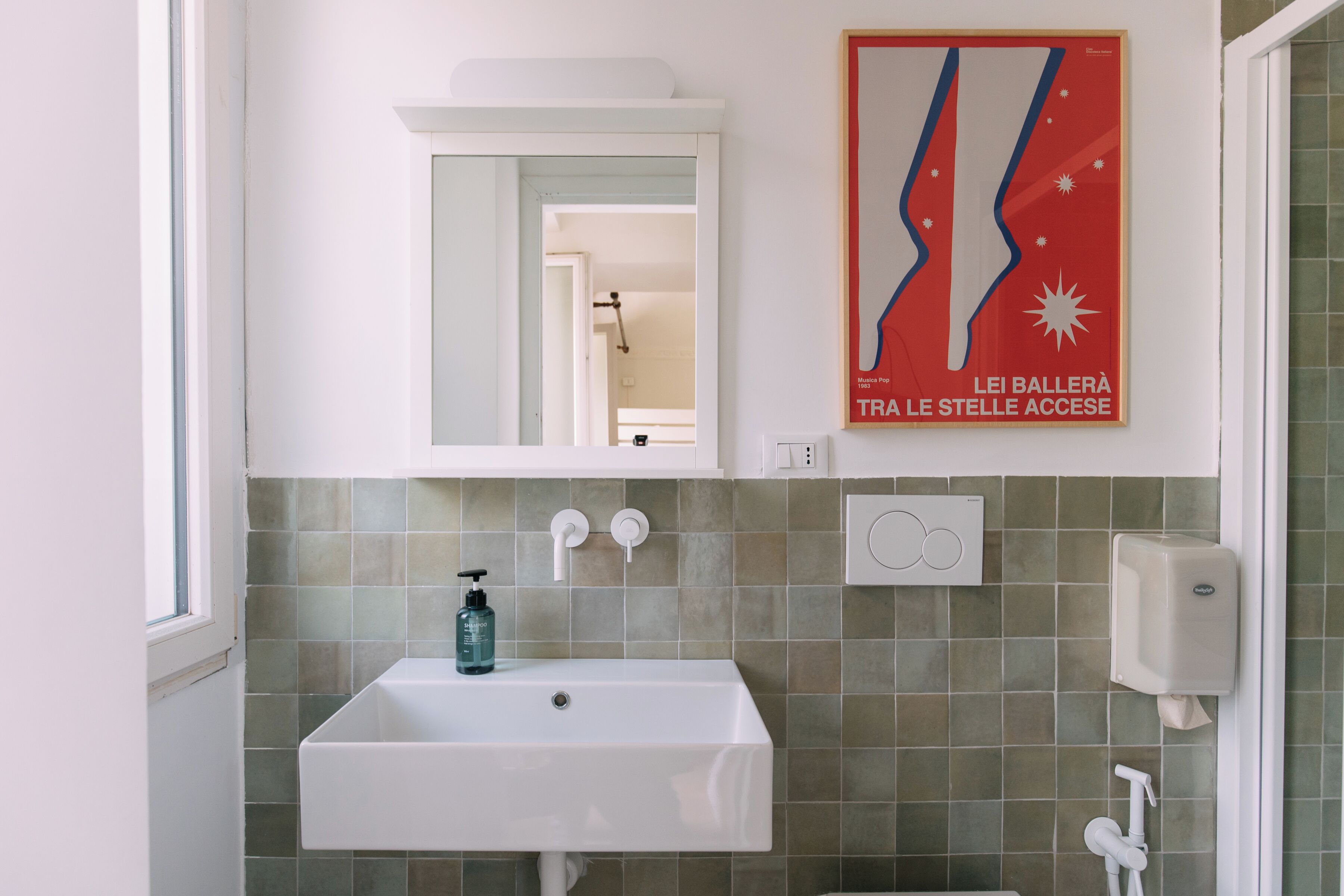 A bathroom with a white sink, a mirror, a poster, and a hand sanitizer dispenser.
