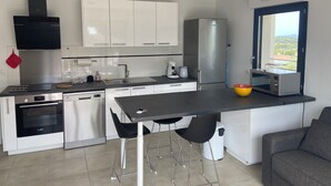 A modern kitchen with a central island, stainless steel appliances, and a view through a window. - New T3 apartment near the sea / port / large terrace / parking (Sanary-sur-Mer)