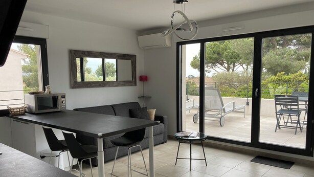 A modern kitchen with a dining area, large sliding glass doors to an outdoor patio, and a small table with a basket. - New T3 apartment near the sea / port / large terrace / parking (Sanary-sur-Mer)