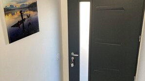 A dark door with a keyhole and a handle, a small mat at the entrance, and a framed picture of a landscape on the wall. - New T3 apartment near the sea / port / large terrace / parking (Sanary-sur-Mer)