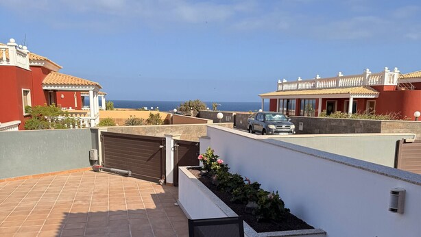 A patio with a wooden table and chairs, a small garden, and a view of the sea and buildings. - Villa Skawi - Cliffside Retreat (Costa de Antigua)