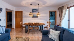 A modern living room with a dining area, white brick walls, wooden furniture, and a large window with curtains. - Villa Skawi - Cliffside Retreat (Costa de Antigua)