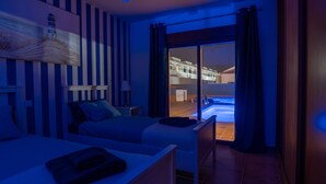 A hotel room with a bed, a desk, a chair, a painting, and a view of a pool and building. - Villa Skawi - Cliffside Retreat (Costa de Antigua)