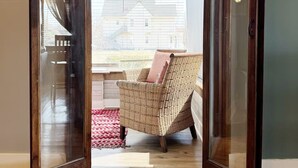 Une pièce avec un fauteuil en osier, un plancher en bois et une vue sur l’extérieur, visible à travers une porte vitrée.