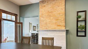 Un coin repas avec une table et des chaises en bois foncé, un mur décoratif en briques, une cheminée blanche et des œuvres d’art encadrées accrochées au mur.