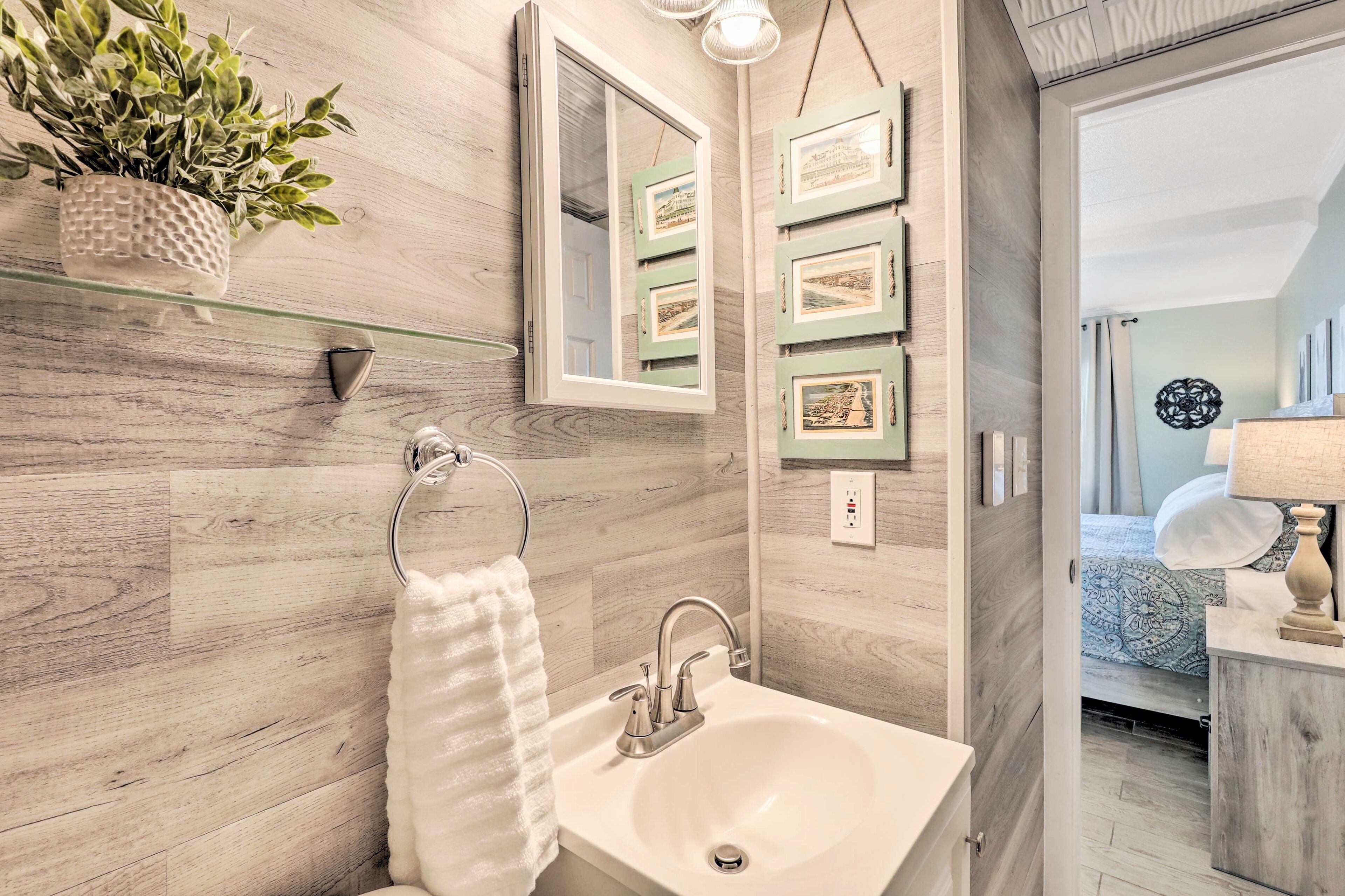A bathroom with a wooden floor, a white sink, a towel rack, a mirror, and framed pictures on the wall.