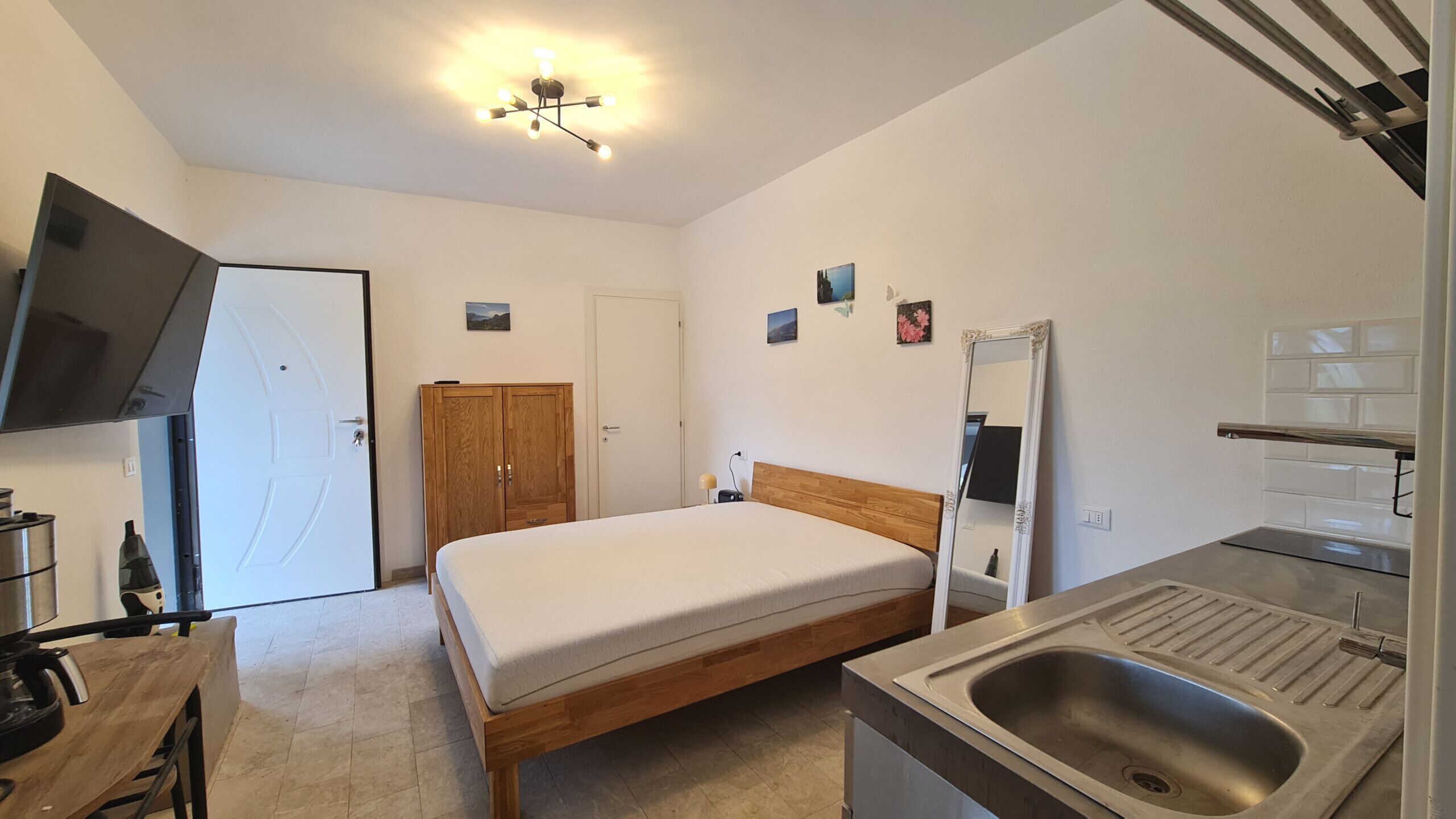 Une chambre à coucher avec un lit, une armoire en bois, une porte blanche, une petite table de chevet et un miroir.