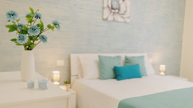 A neatly arranged bedroom with a bed, bedside tables, a vase with flowers, and wall art. - Modern and functional space in the heart of the city (Mazara del Vallo)