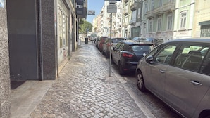 A narrow cobblestone street lined with parked cars and buildings. - Hostel Benformoso (Lisbon)