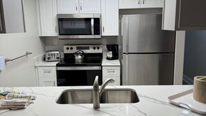 Une cuisine moderne avec des meubles blancs, un réfrigérateur en acier inoxydable, un four à micro-ondes et une cuisinière à gaz.