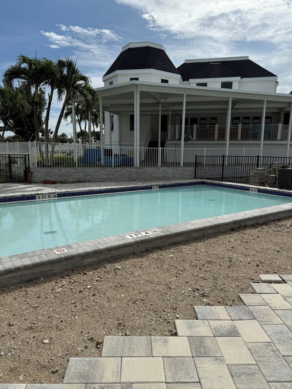 A swimming pool with a white fence, a covered area with a roof, and palm trees in the background.