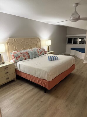 Ein Schlafzimmer mit Bett, Nachttischen, einer Lampe, Deckenventilator und einem Fenster mit Jalousien.