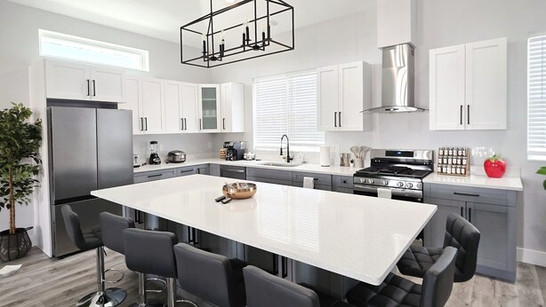Een moderne keuken met een centraal eiland, barkrukken, roestvrijstalen apparatuur en een hanglamp.