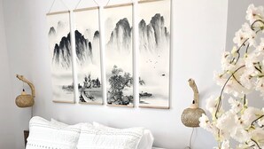 Een slaapkamer met een bed, wit beddengoed, een houten hoofdbord, een wandlamp en een decoratief hangend object.