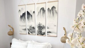 Une chambre à coucher avec un lit, du linge de lit blanc, une tête de lit en bois et trois tableaux accrochés au mur représentant des paysages.