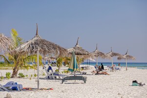 Una playa con sombrillas de paja, sillas de descanso y una orilla arenosa.