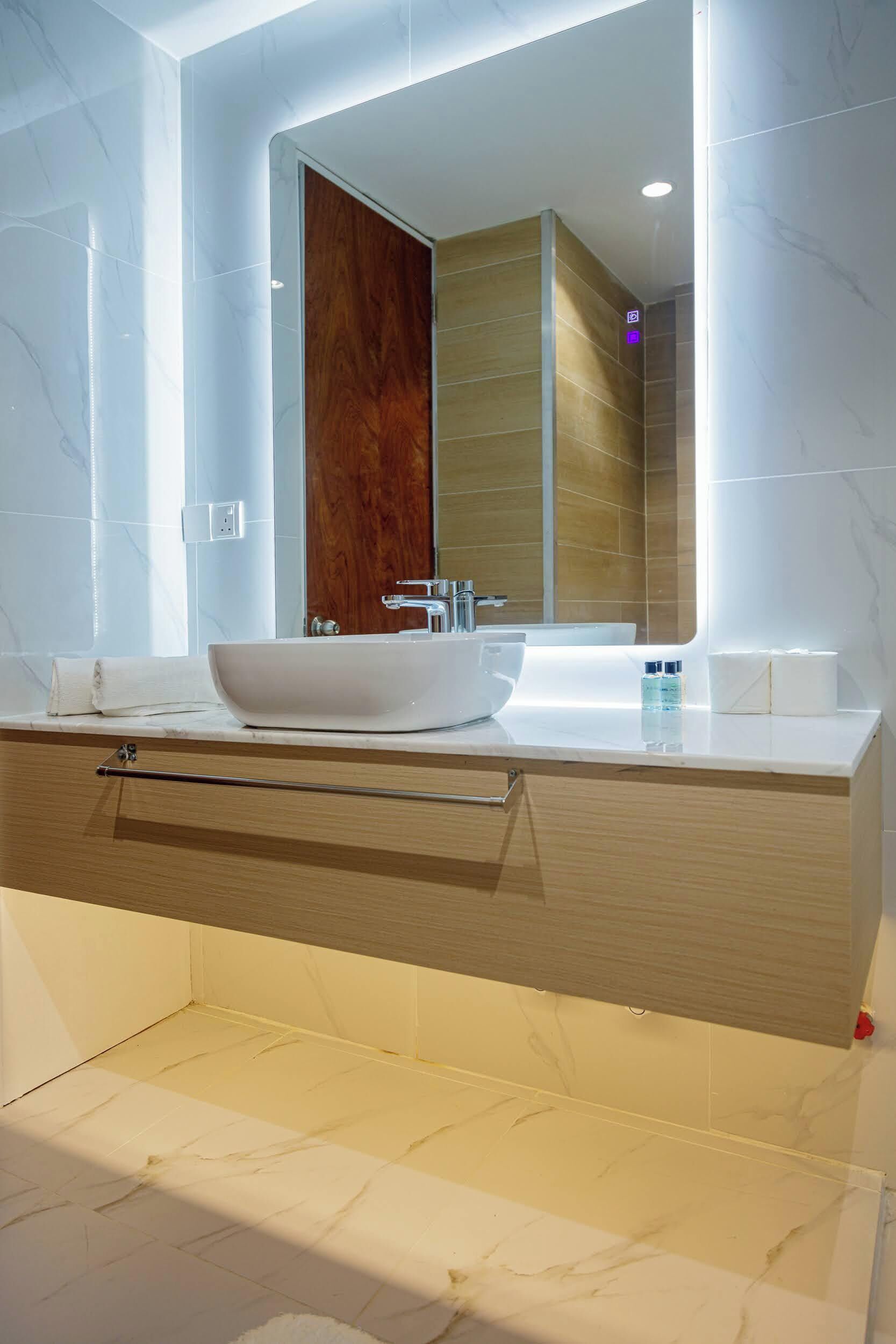 A modern bathroom with a large mirror, a white sink, and a wooden vanity.