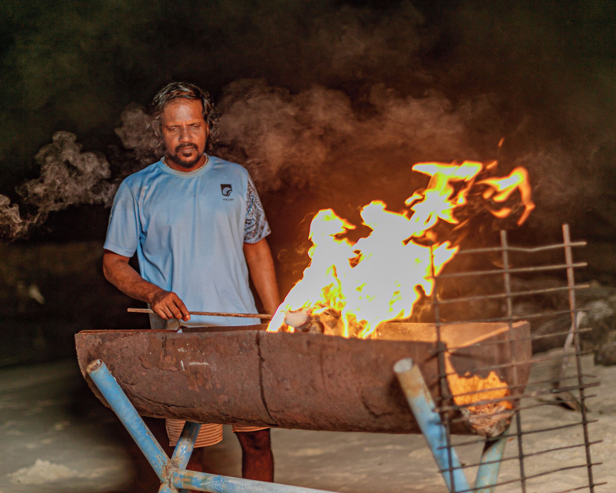 A person standing next to a large fire burning in a metal container.