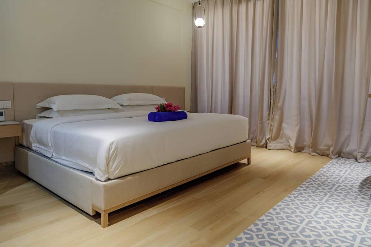 Una cama bien tendida con sábanas blancas, una bandeja azul con flores y suelo de madera.