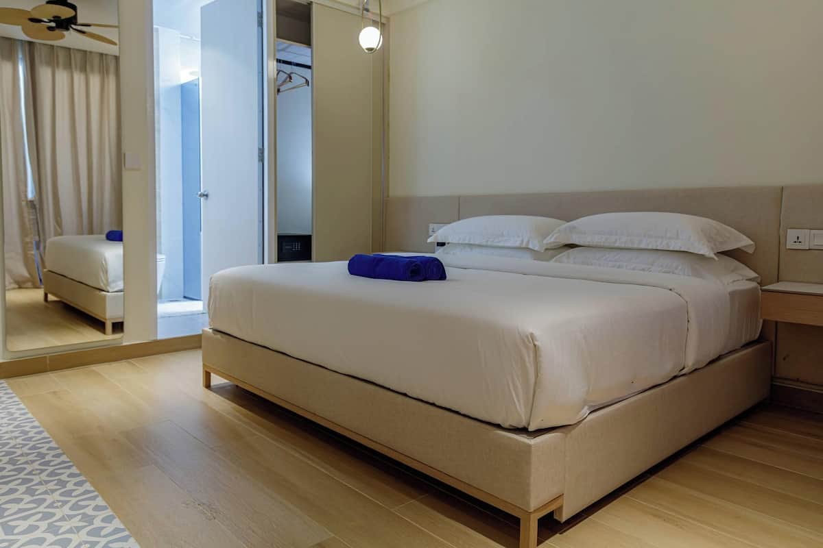 Habitación de hotel con una cama grande, una mesita de noche, un espejo y un ventilador de techo.