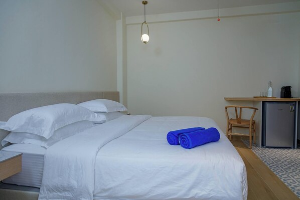 A hotel room with a bed, a desk, a chair, and a refrigerator.