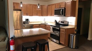 A kitchen with wooden cabinets, stainless steel appliances, a granite countertop, and two stools.