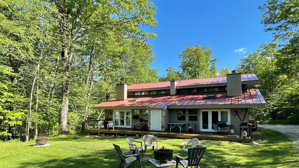 A two-story house with a red roof, surrounded by a grassy lawn and trees.