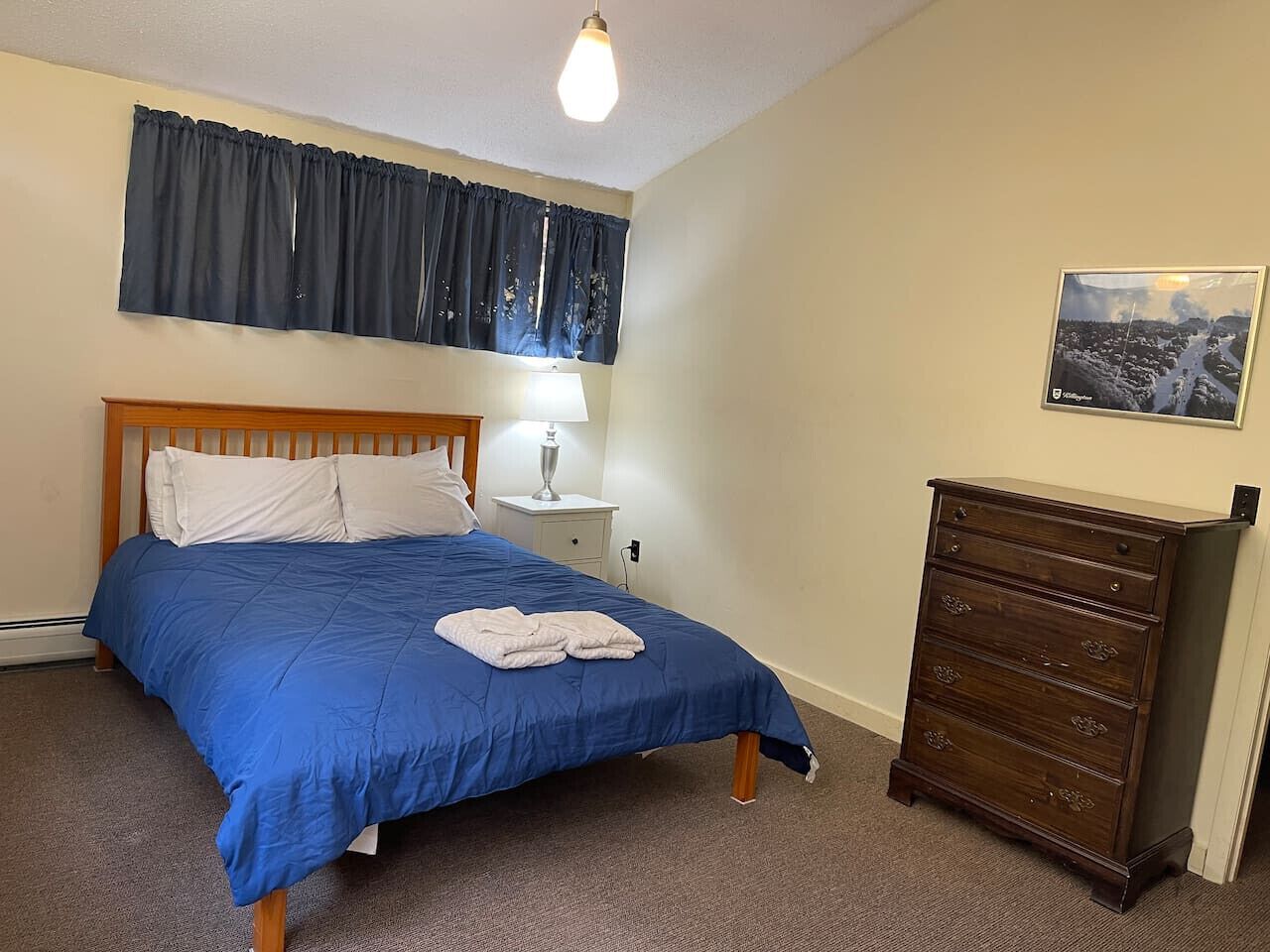 A bedroom with a bed, a nightstand, a dresser, a lamp, and a picture on the wall.