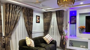 A modern living room with a sectional sofa, a glass coffee table, and a TV mounted on the wall. - Arek Condos- Your Charming Tropical Home Away from Home in the Heart of Accra. (Greater Accra Region)