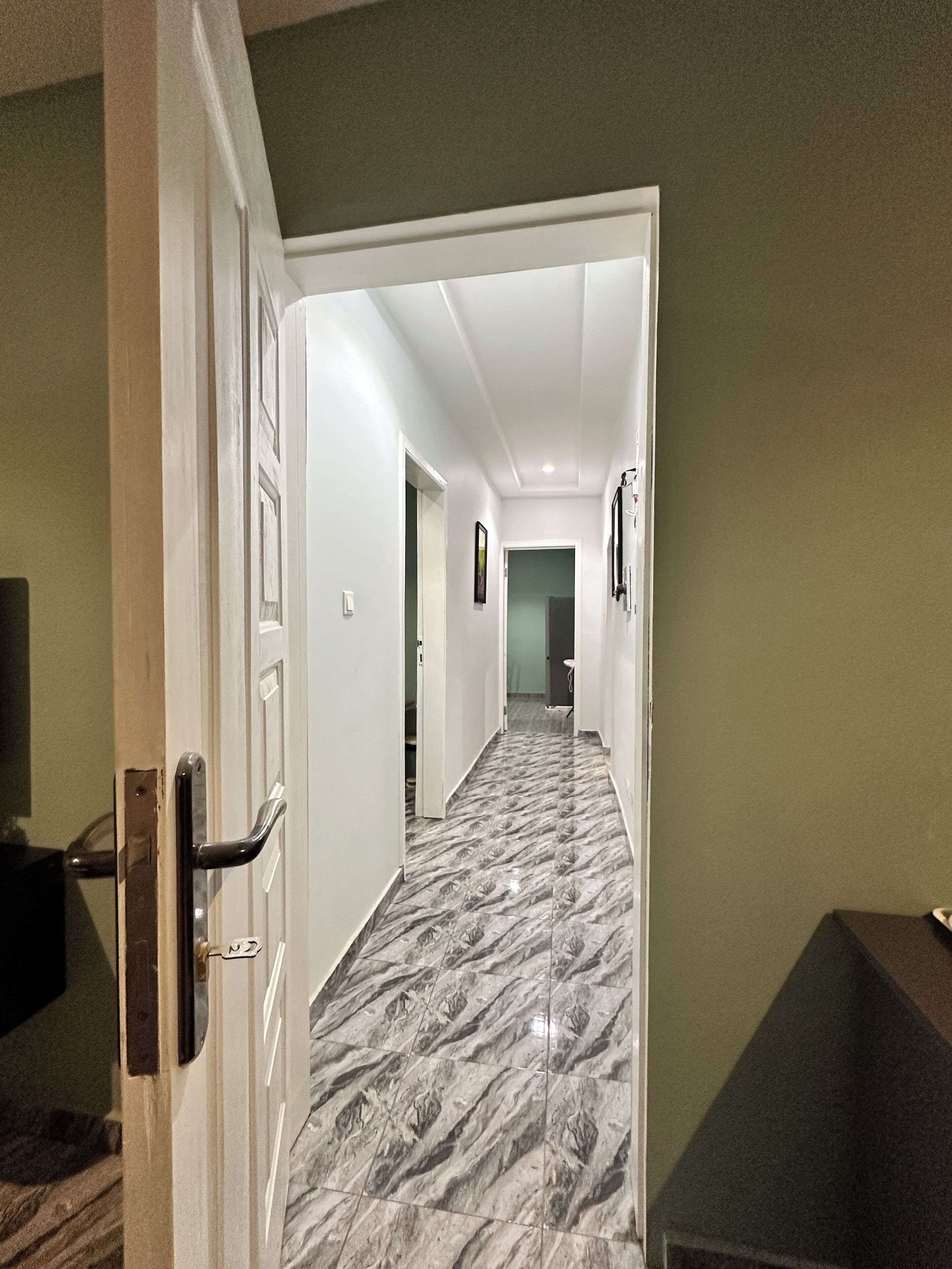 A hallway with a marble floor, white walls, and a door on the left.