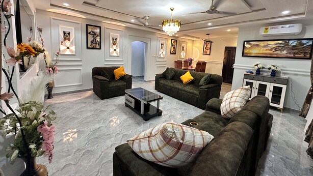 A modern living room with two sofas, a coffee table, and a chandelier. There are wall-mounted lights and a ceiling fan. - Arek Condos- Your Charming Tropical Home Away from Home in the Heart of Accra. (Greater Accra Region)