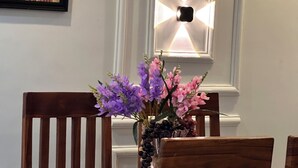 A framed artwork of a person in traditional attire, a wall-mounted light fixture, and a vase with purple flowers. - Arek Condos- Your Charming Tropical Home Away from Home in the Heart of Accra. (Greater Accra Region)