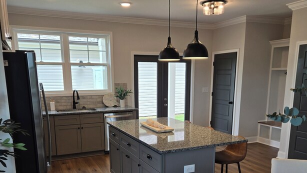 A modern kitchen with granite countertops, a central island, pendant lighting, and a dining area with a wooden table and chairs.