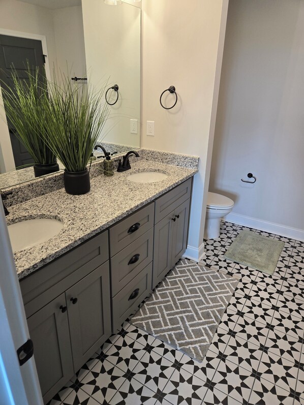 Un baño con encimera de granito, un lavabo, un espejo, un inodoro y un suelo con diseño.