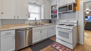 A modern kitchen with white cabinets, stainless steel appliances, and a window with blinds.