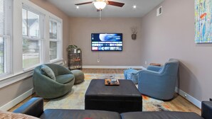 A living room with a ceiling fan, a flat-screen TV, and modern seating including a bean bag and a lounge chair.