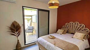 A bedroom with a bed, a large mirror, a wicker headboard, and a view to an outdoor area.