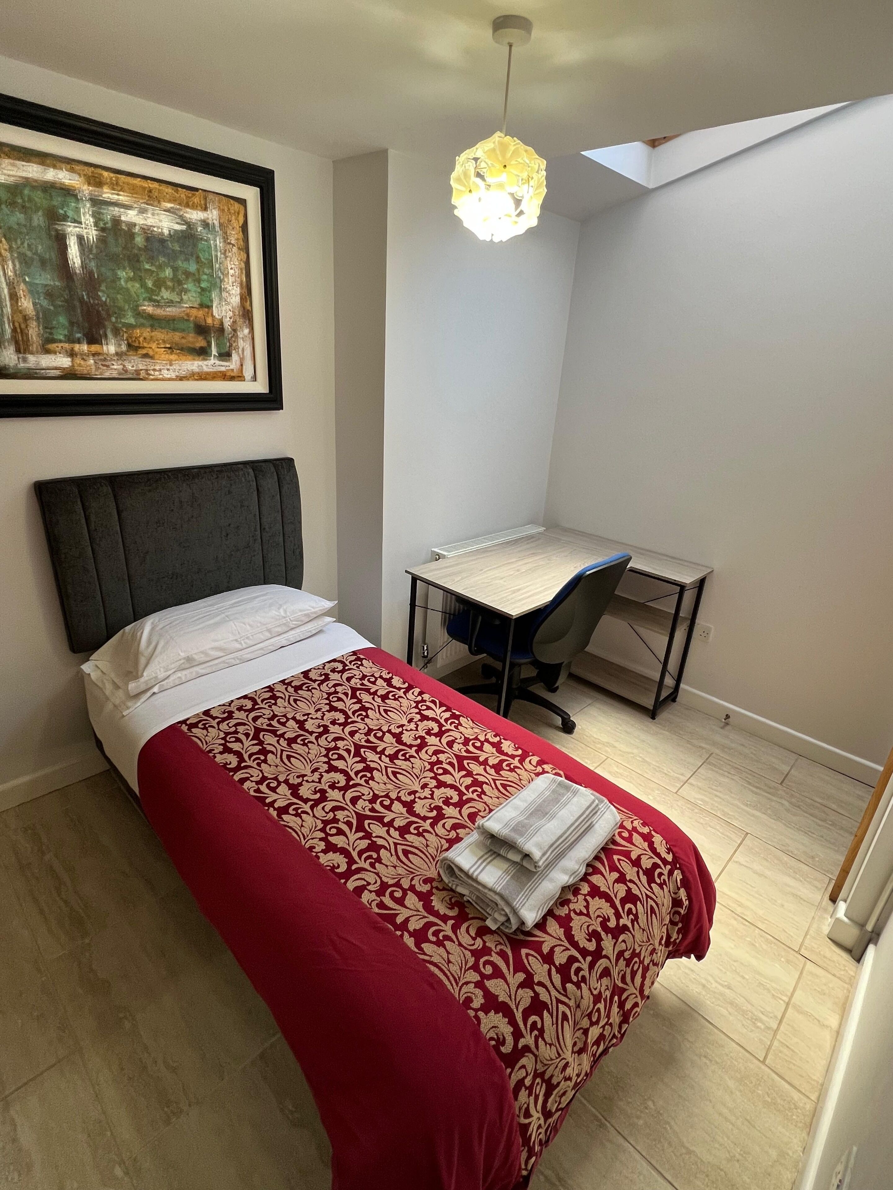 A bedroom with a bed, a desk, and a painting on the wall.