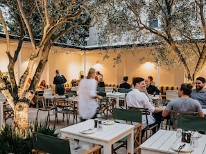 An outdoor dining area with tables and chairs, surrounded by trees and a building in the background. - Absolute Beachfront Luxury (Bondi Beach)