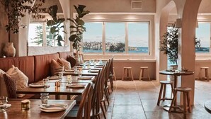 Ein Restaurant mit einem langen Esstisch, gepolsterten Sitzgelegenheiten und Blick auf das Meer.