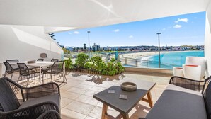 Eine Dachterrasse mit Blick auf Strand und Stadtlandschaft, möbliert mit Korbstühlen und Tischen.