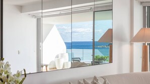 Ein modernes Wohnzimmer mit einem großen Fenster, das auf einen Balkon mit Meerblick blickt.