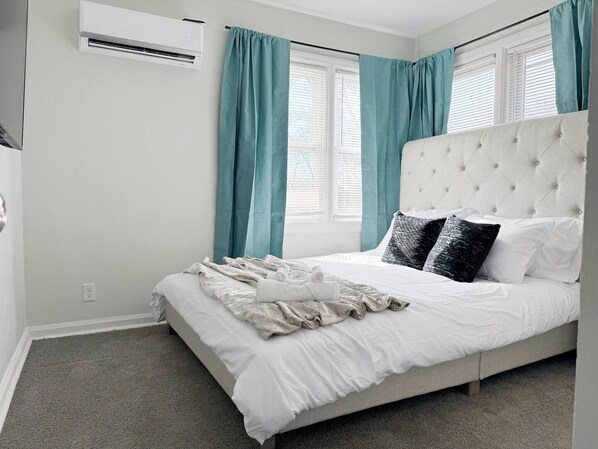 Een slaapkamer met een groot bed, een wit hoofdeinde en turquoise gordijnen.