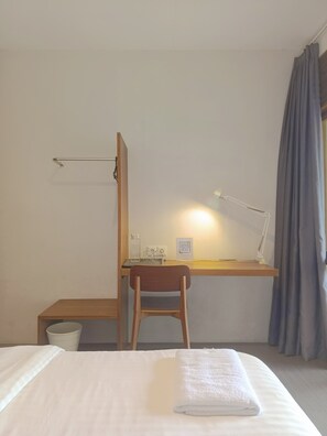 A hotel room with a bed, a desk with a chair, a desk lamp, a small table with a glass, and a QR code on the wall. - Habitat Hills by Santai Aja (Cisarua)