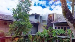 A courtyard with a water feature, surrounded by tropical plants and trees, and modern buildings with tiled roofs. - Habitat Hills by Santai Aja (Cisarua)